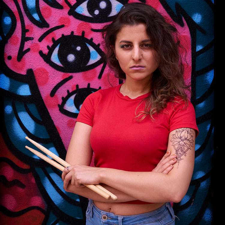 photo of Mirna Ayshoa in front of a graffiti wall holding sticks